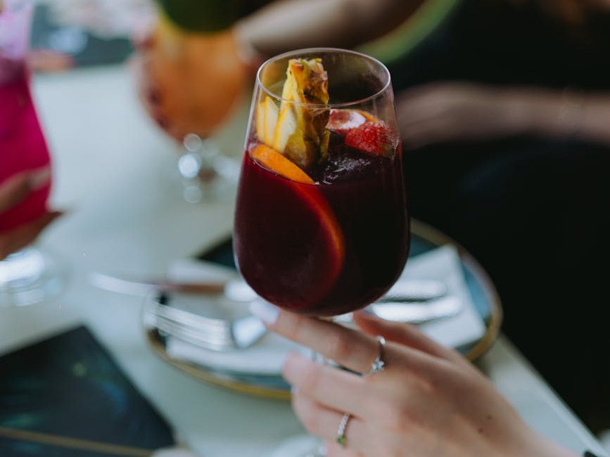 A person holding a wine glass with red wine and pieces of fruit in it