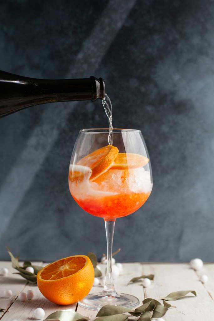 An orange cocktail being poured into a wine glass