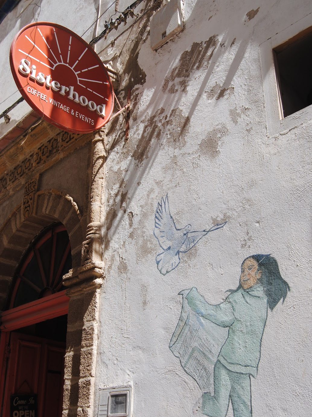 A sign that says "Sisterhood" above a small mural of a woman and a dove