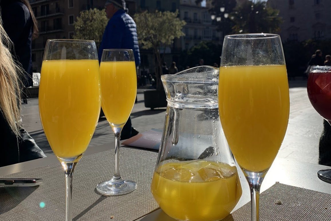 Three glasses and a pitcher of Agua de Valencia, an orange-colored Spanish cocktail