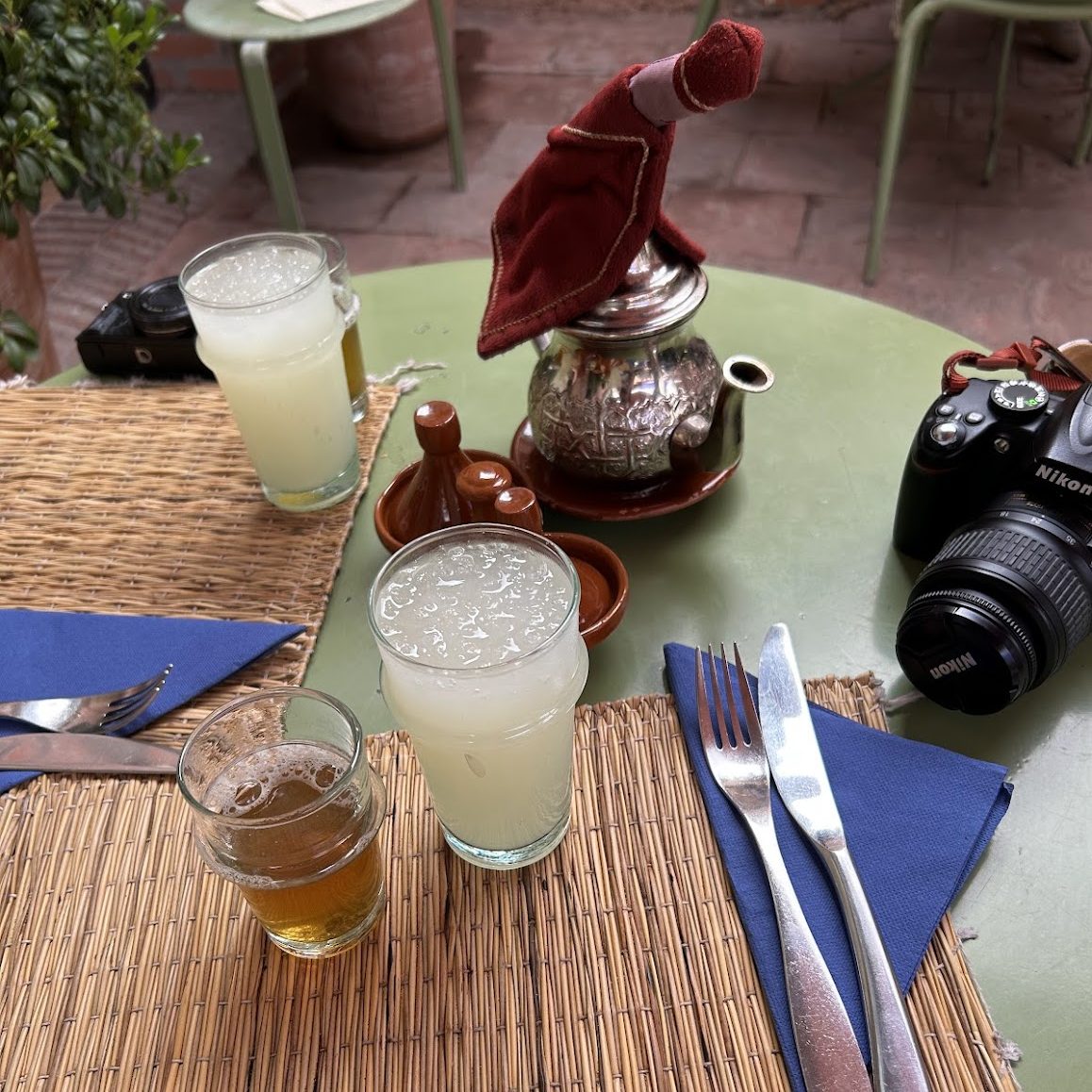 A table with several cups of tea and lemonade, and two cameras