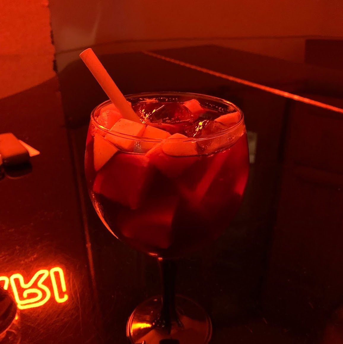 A glass of sangria sitting on a table in a dark room with red lighting