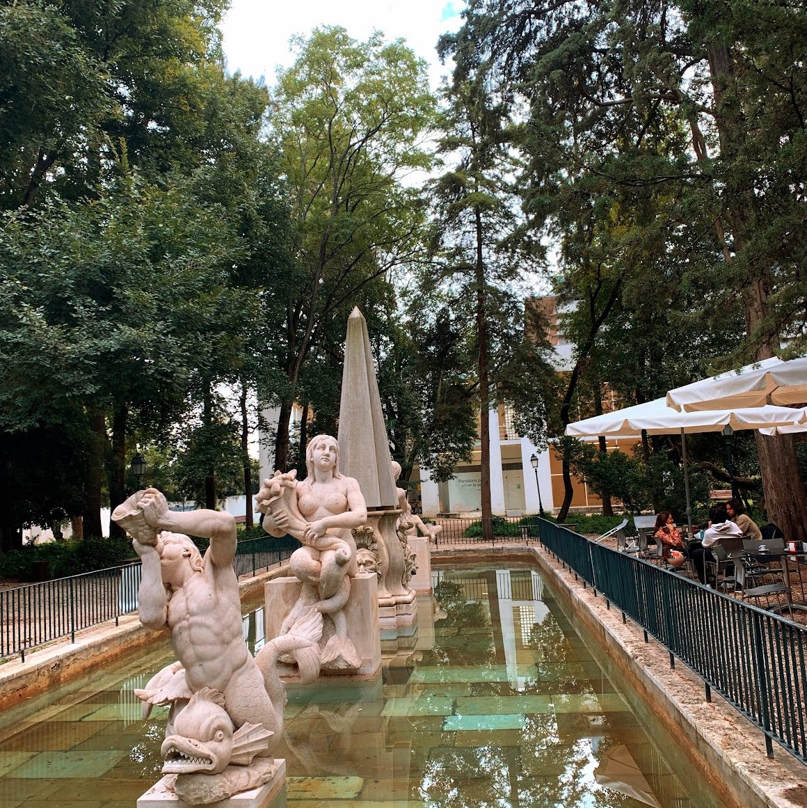 Statues in a large fountain next to a cafe