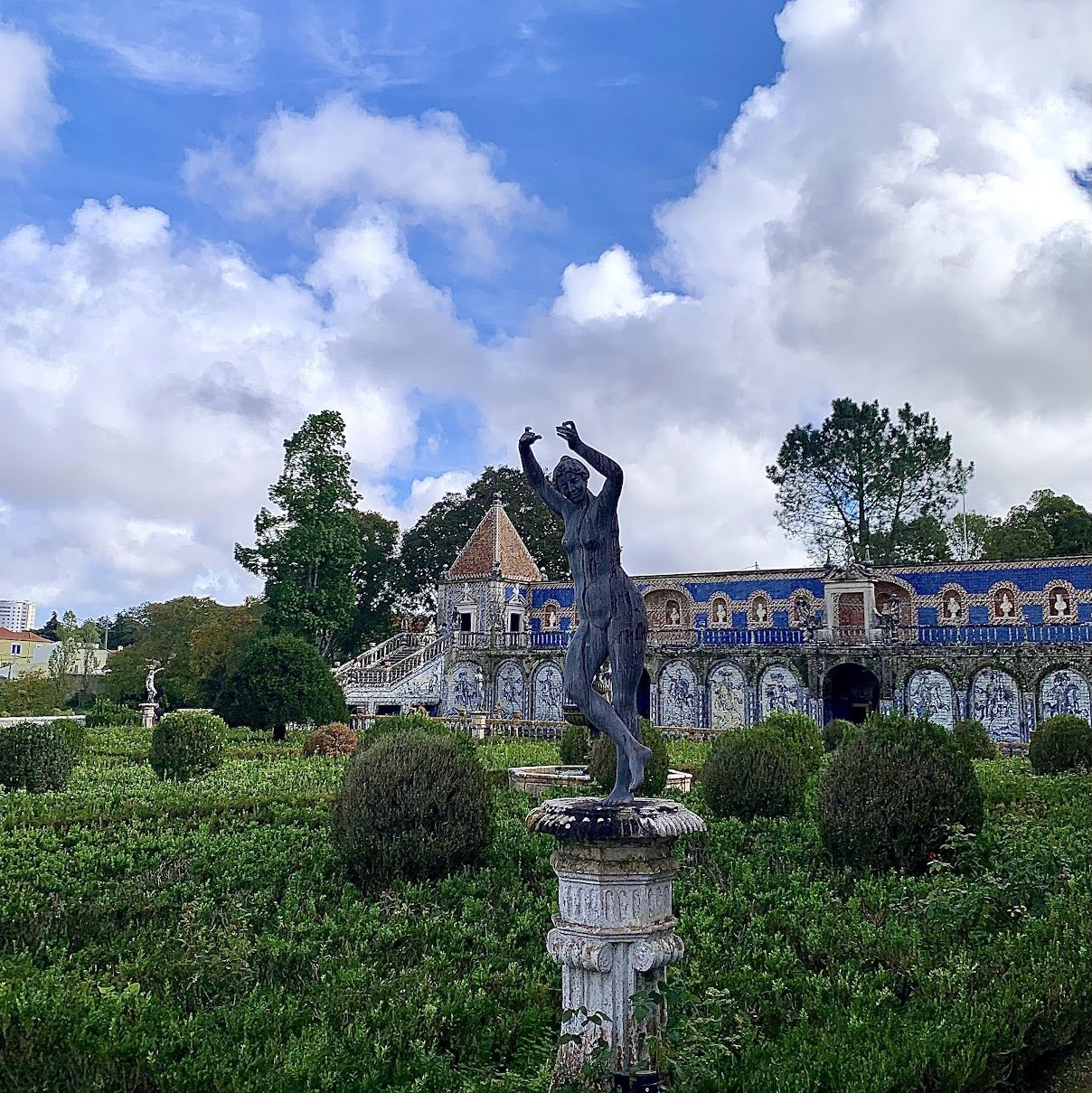 A statue of a woman with her arms raised in a palace garden