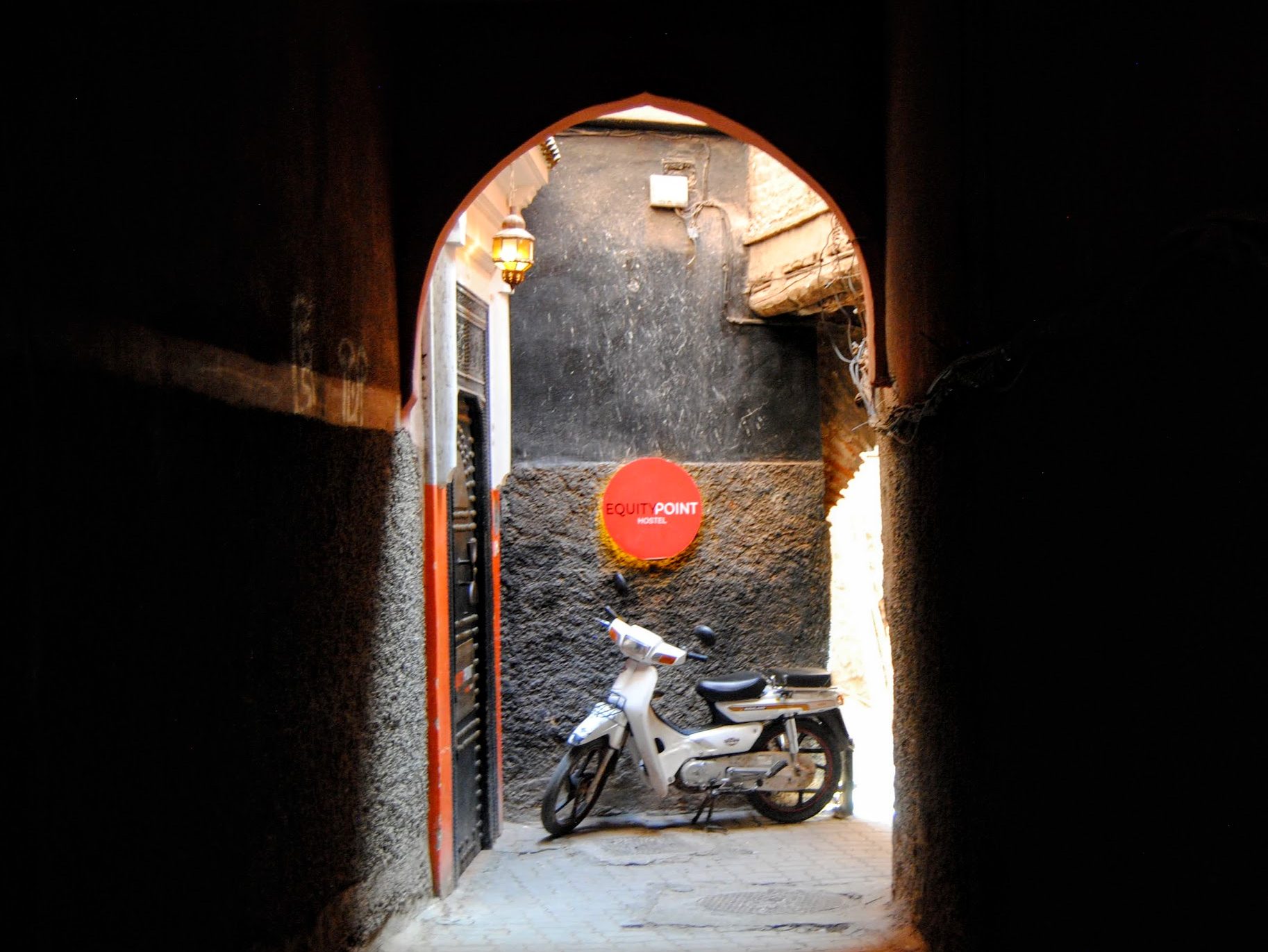 A white motorcycle under a small hostel sign at the end of a corridor  